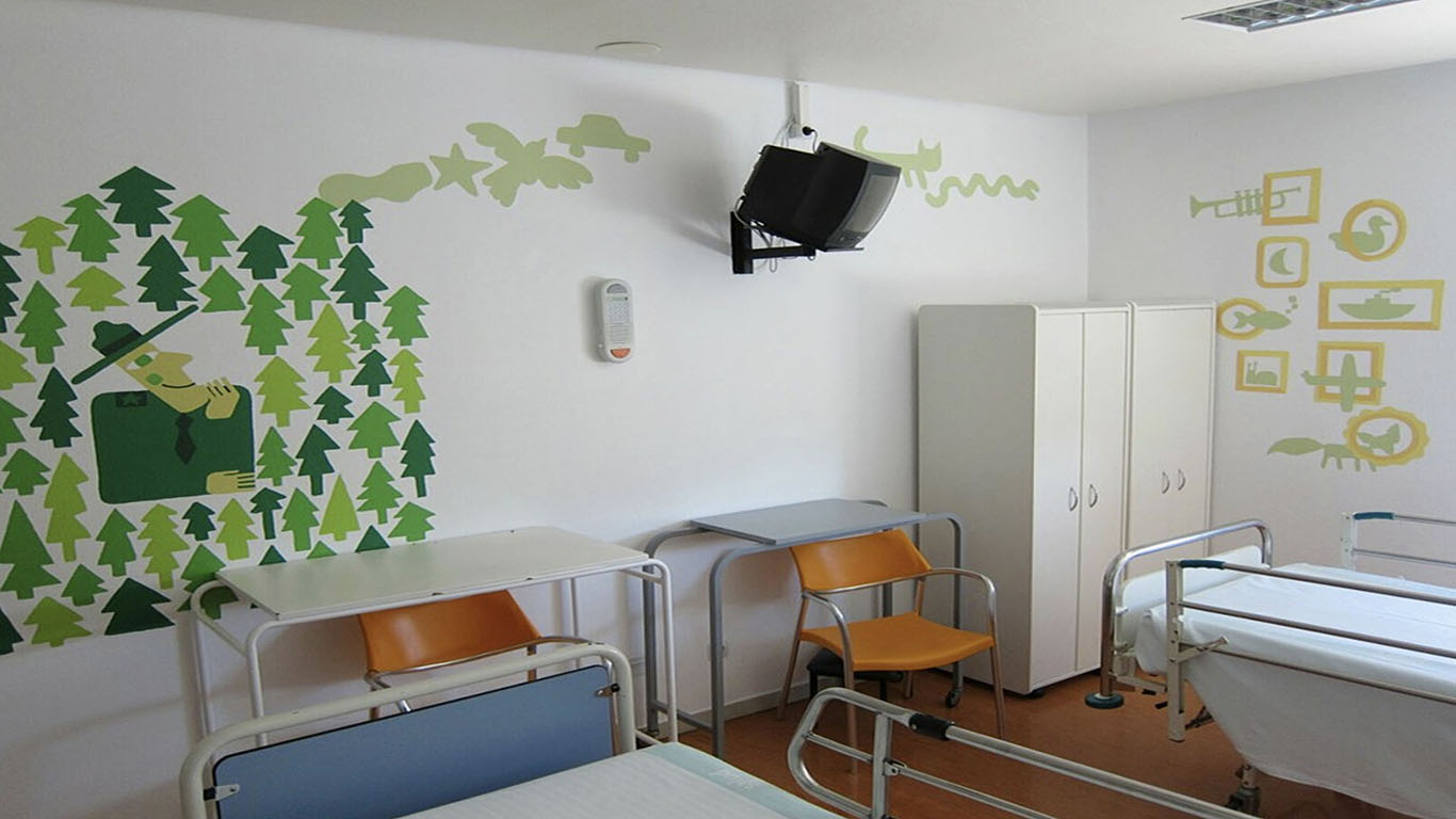 Ilustración realizada en una habitación del Hospital Infantil de Zaragoza. En ella se ve una casa construida con árboles verdes y expulsando por la chimenea diversas figuras. 