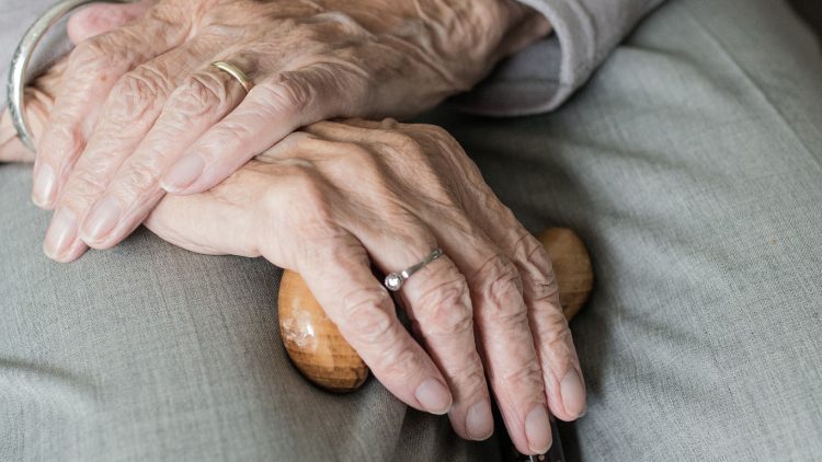 una anciana con las manos cruzadas mientras mantiene un bastón